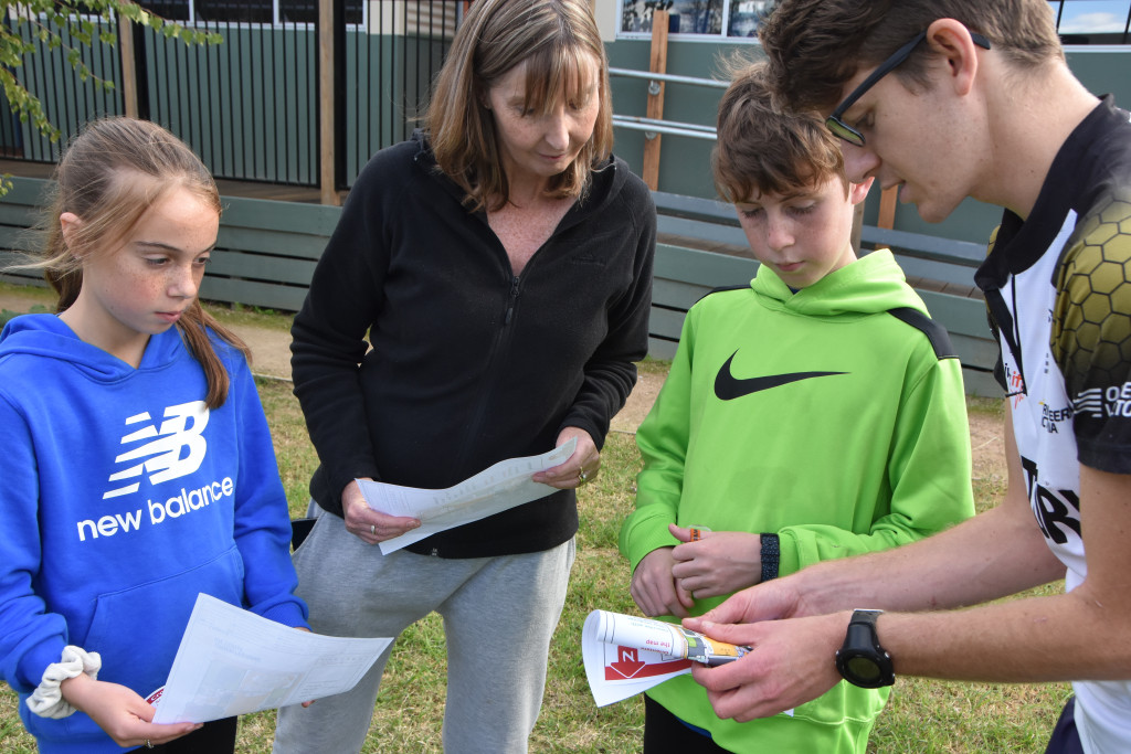 Family of orienteers being shown how to fold a map by a coach