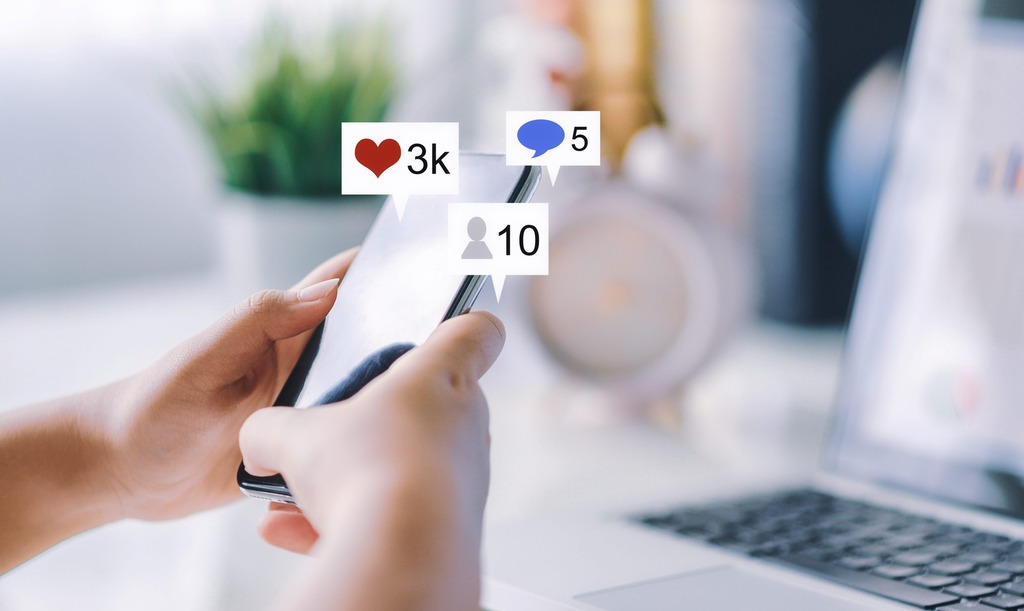 Hand holding a phone with social media icons floating out of phone