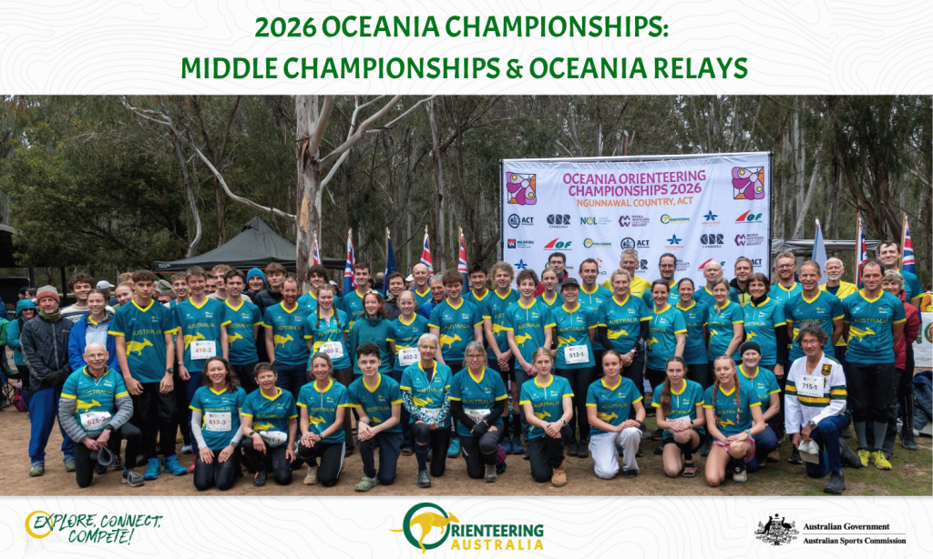 Group of athletes in turquoise Australia shirts posing for a photo at the 2026 Oceania Championships, with a banner behind them and flags nearby.