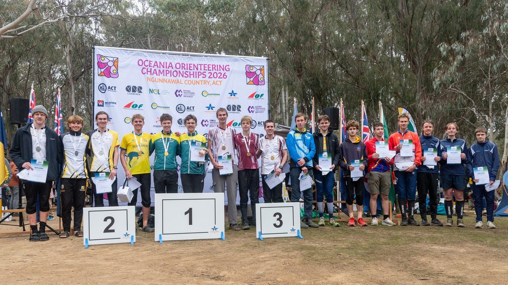 Group of young athletes on podiums with medals and diplomas at the Oceania Orienteering Championships 2026 awards ceremony.